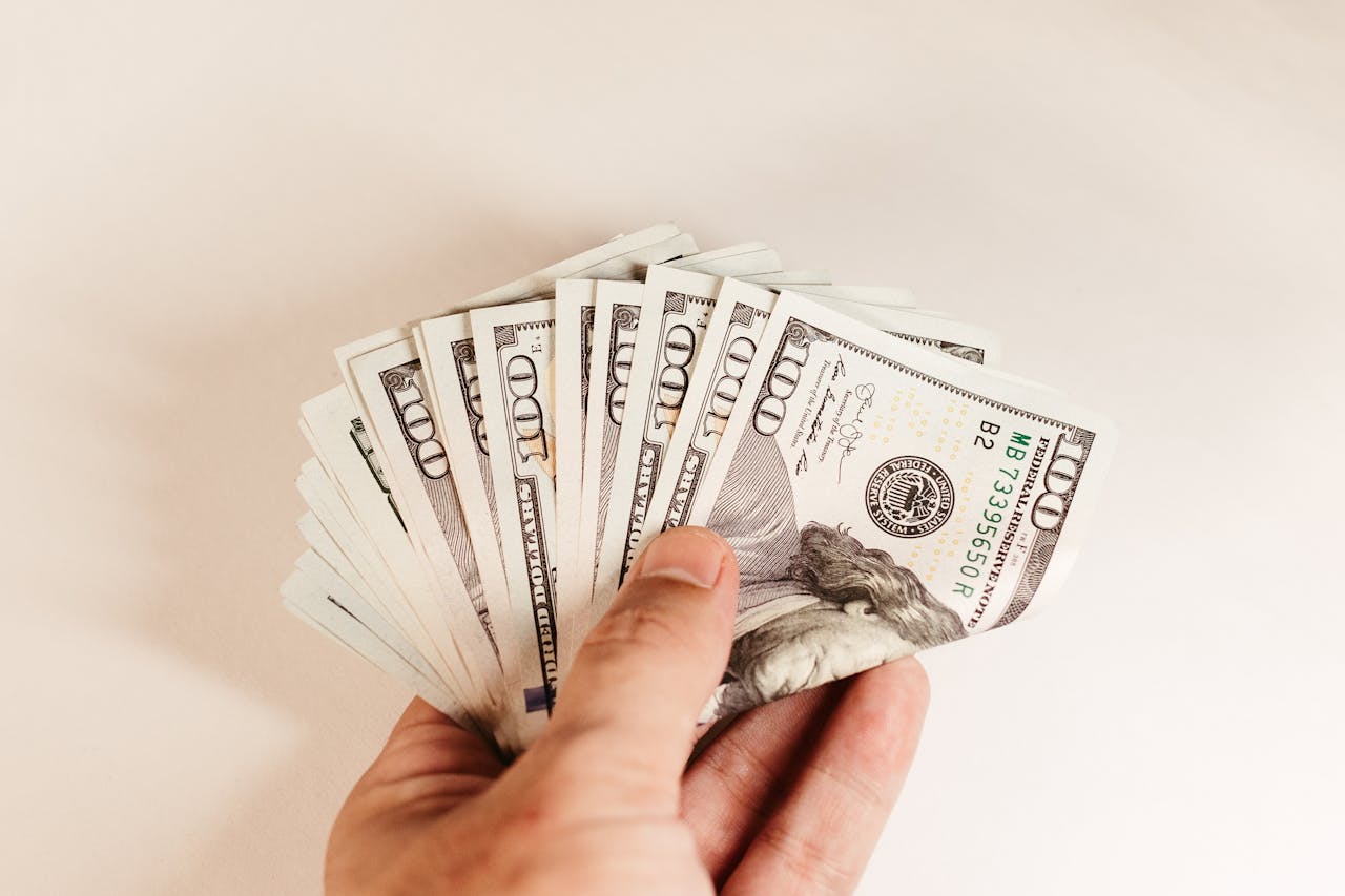 about-02 Close-up of a hand holding US hundred-dollar bills on a white background.